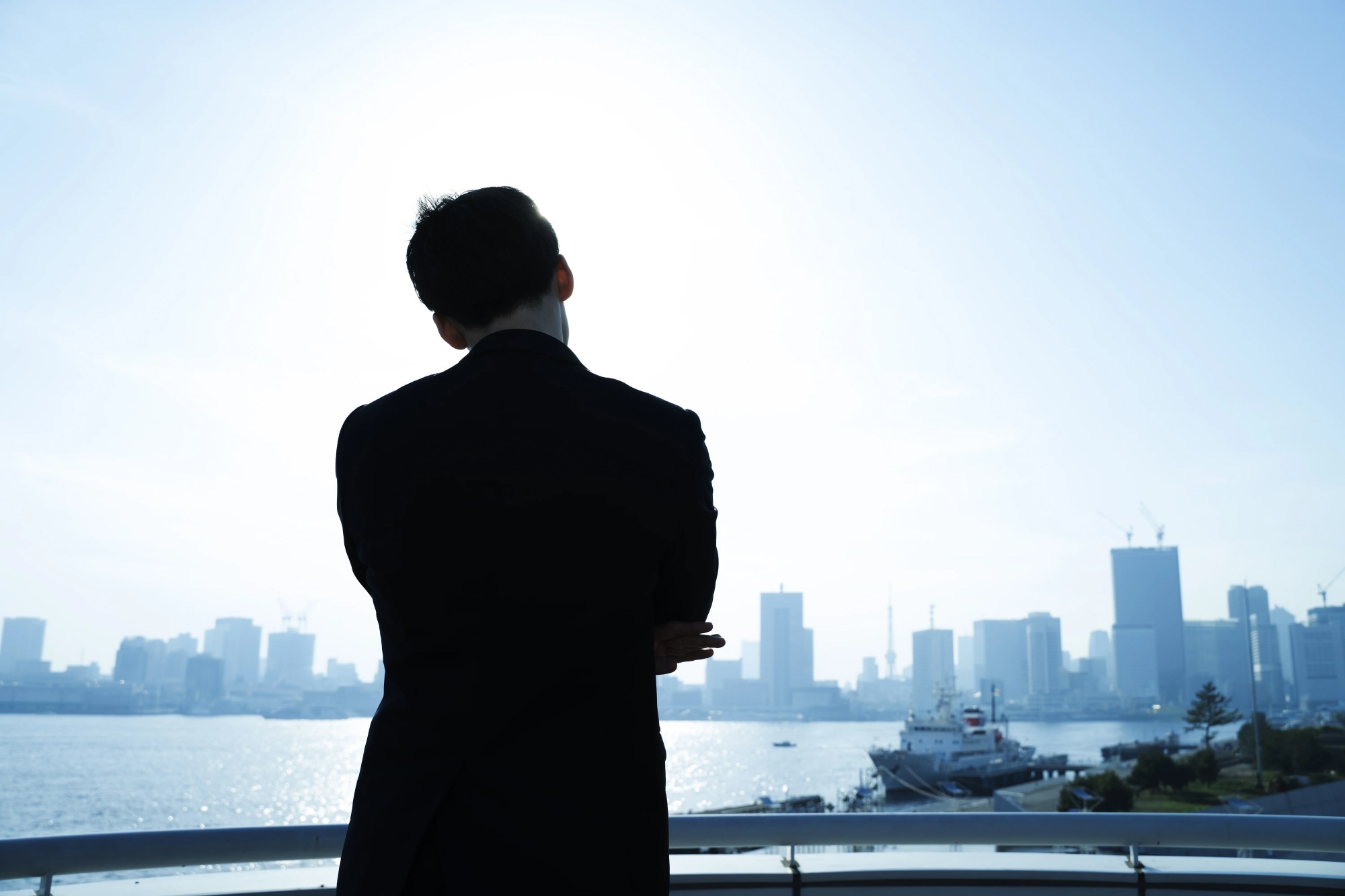 「考える」のイメージ_腕を組んで考え込む男性の後ろ姿