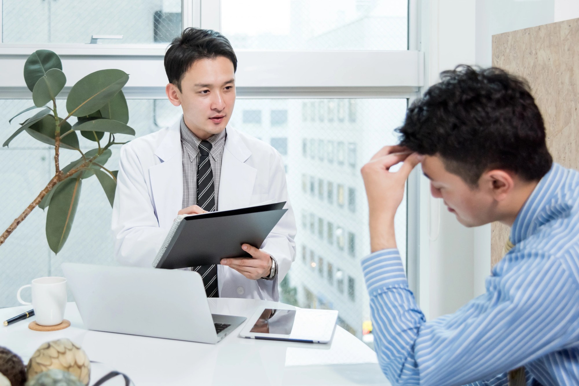「診療」のイメージ_頭を抱えて辛そうな男性と、真剣に話をしている医師