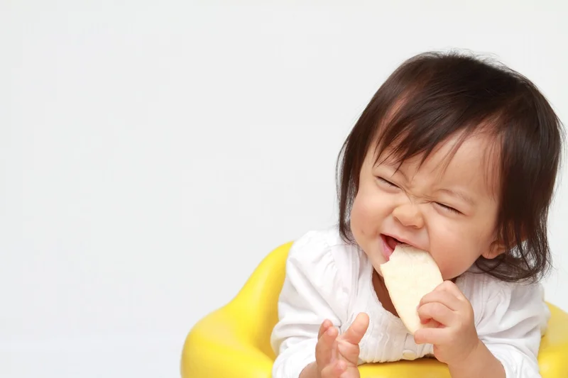 「赤ちゃんのおやつ」のイメージ_笑顔でおせんべいを食べている赤ちゃん