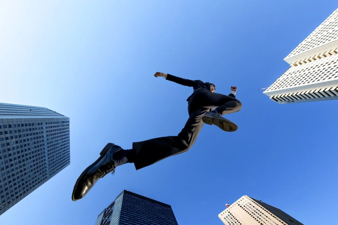 「成功」のイメージ_ビルの合間を男性がジャンプで駆け抜ける様子