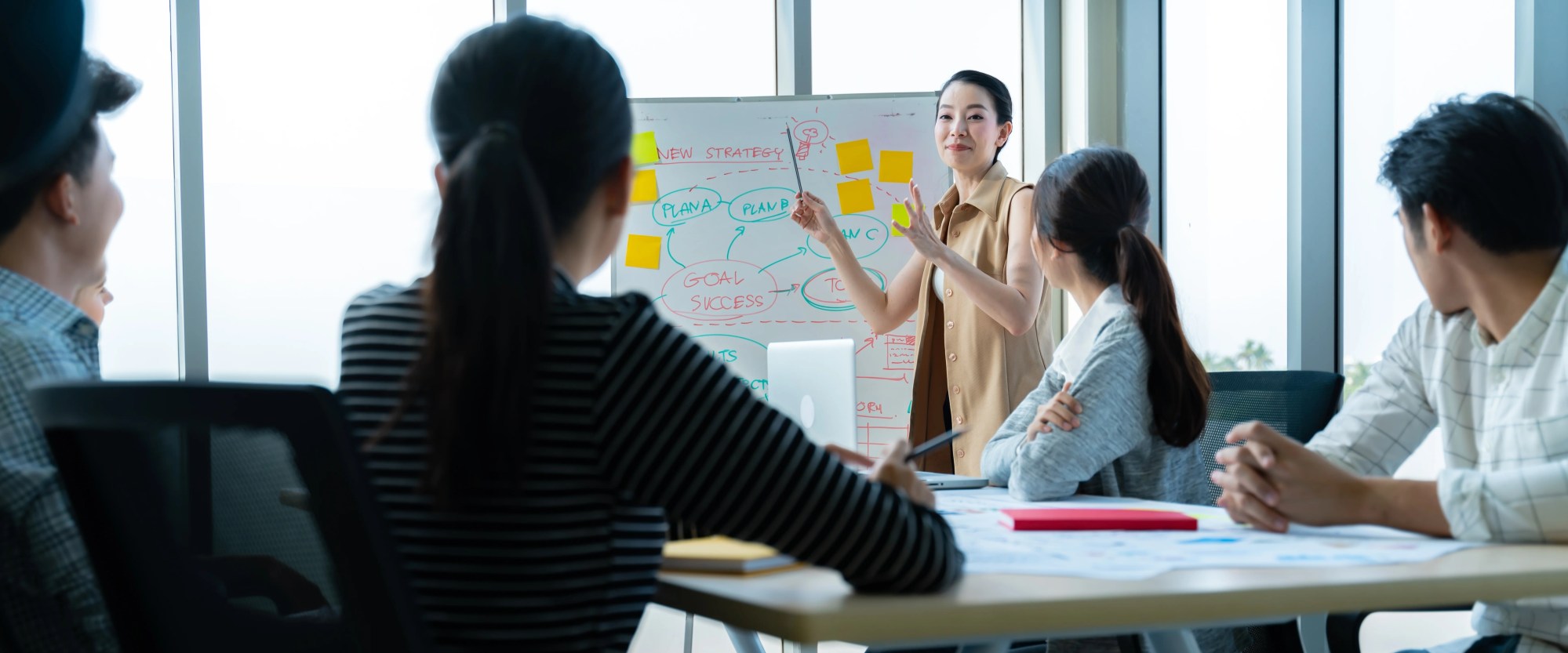 「プレゼン」のイメージ_プレゼンをしている女性と真剣に話を聞く複数名の社員