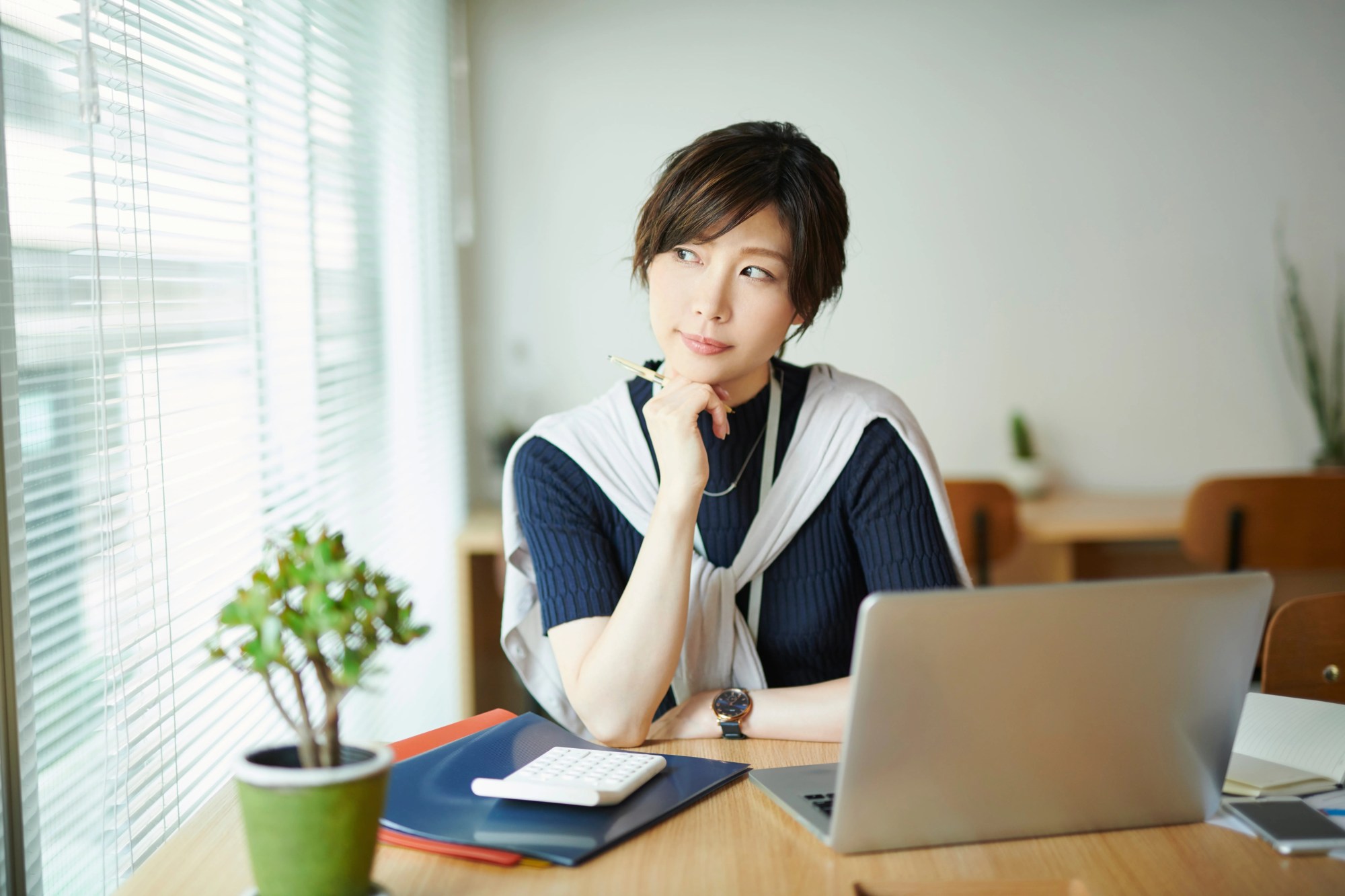 「考える」のイメージ_パソコンの前で顎に手をあて、考え込む女性