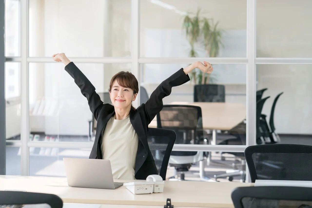 「快適」のイメージ_デスクで気持ちよさそうに伸びをする女性
